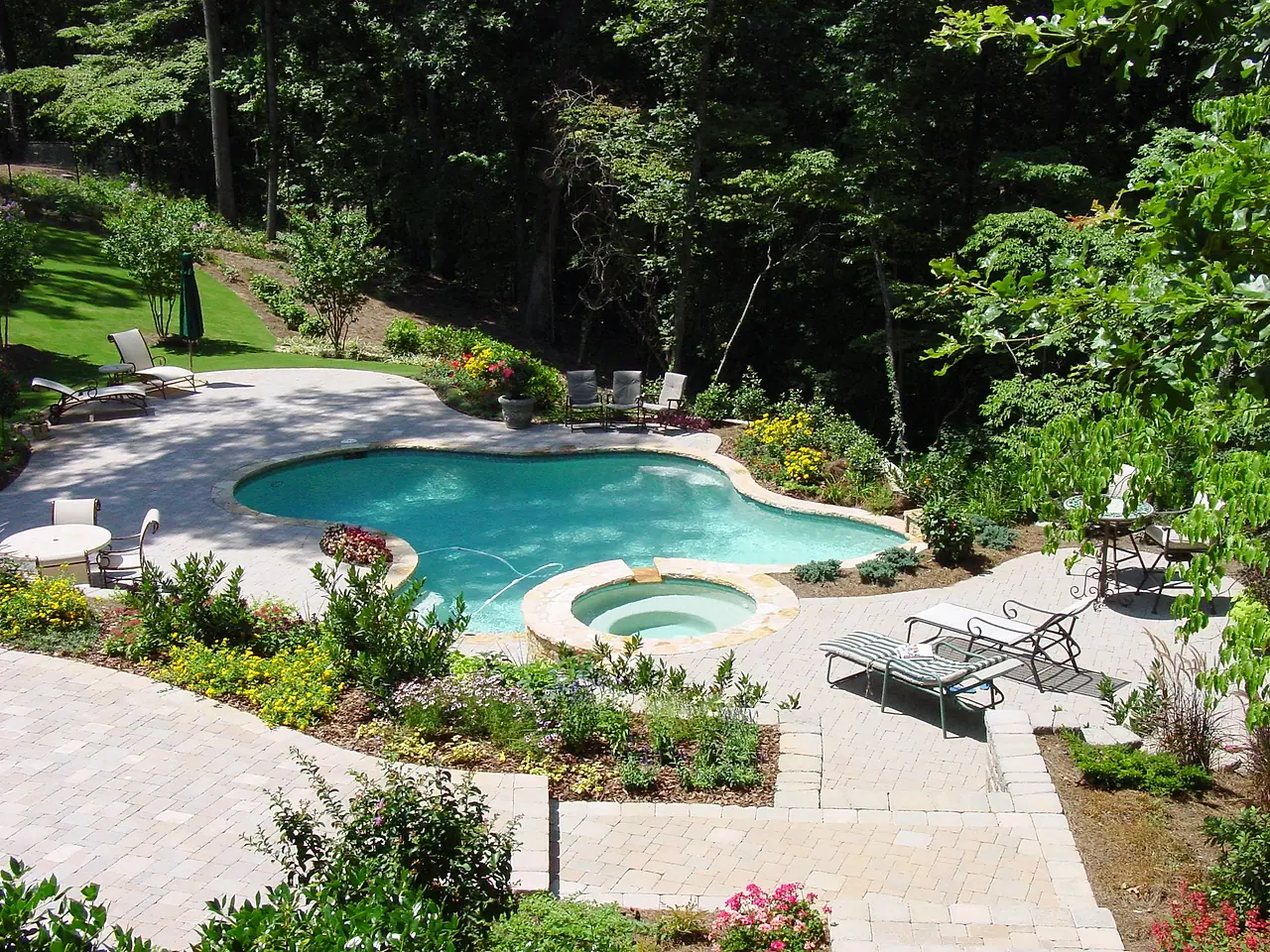 Freeform pool and spa with a paver deck and flower beds